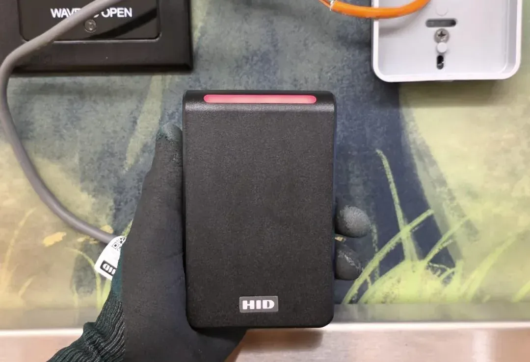 HID access-control reader beside a request-to-exit button, with the door wiring visible.