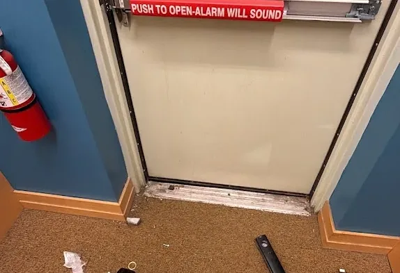 Commercial exit door with a horizontal panic bar and service tools nearby.