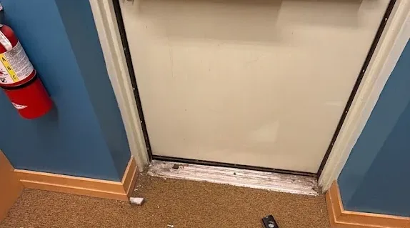 Commercial exit door with a horizontal panic bar and service tools nearby.