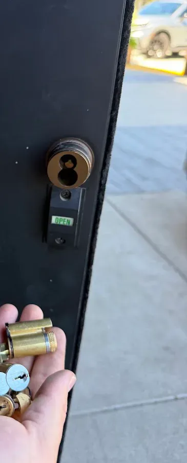 Technician holds a removed brass cylinder beside the open lock on a commercial door