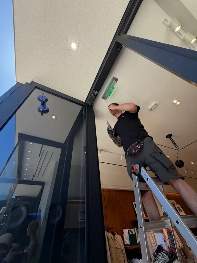 Technician working from a ladder at a commercial entrance.