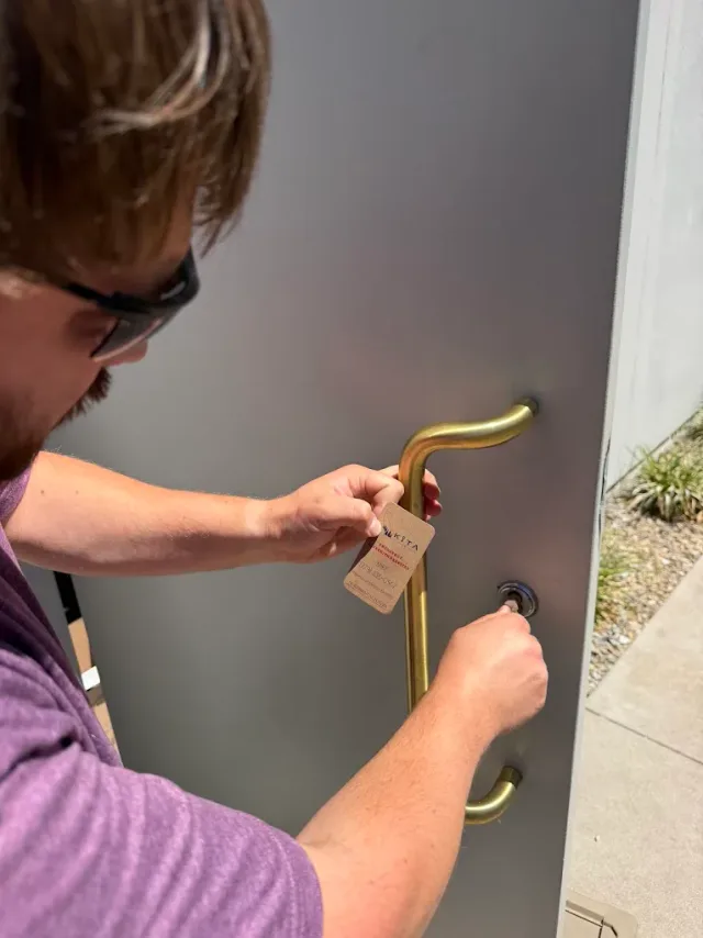 Technician tightening entry-door hardware outside a building.