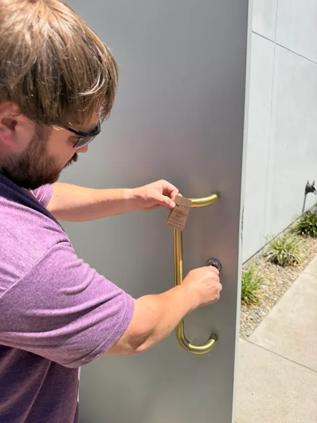 Technician fitting door hardware at an exterior entry.